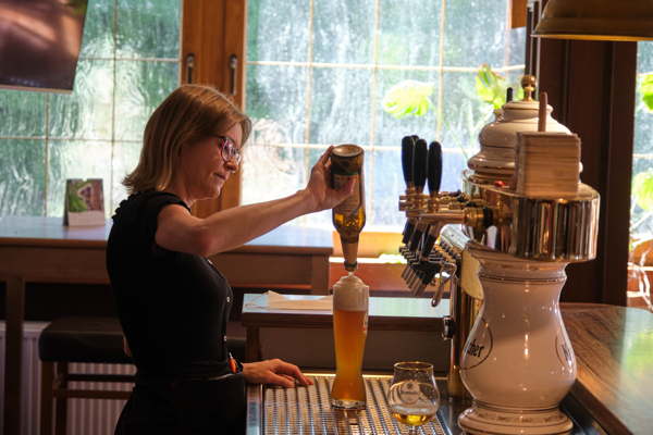 Eine junge Frau zapft ein frisches Bier, das ist gesellig und man hat schnell Kontakt zu anderen Menschen an der Theke.